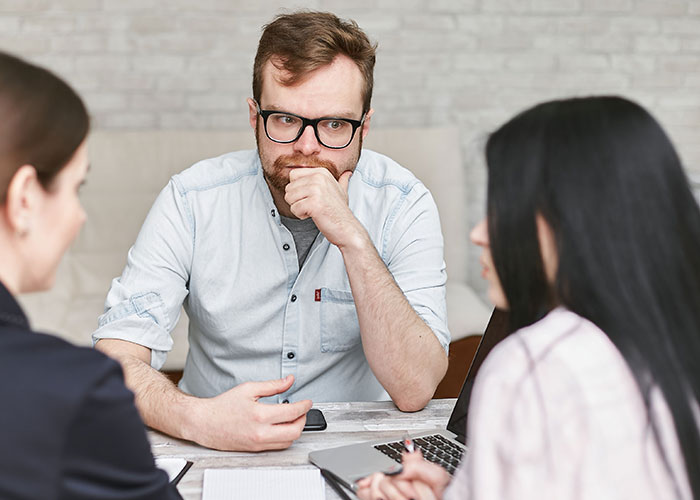 A man in glasses listening intently during a job interview, perhaps hearing a hilarious story.