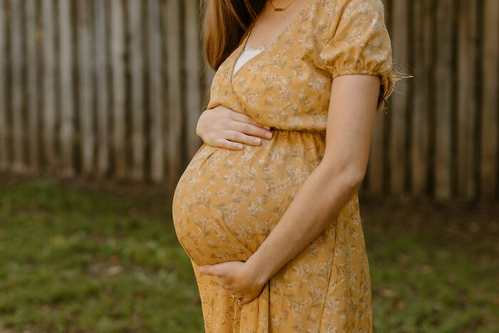 A pregnant woman in a yellow floral dress cradling her belly, symbolizing new beginnings in Last Will Stories.