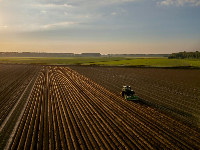 An aerial view of a tractor tilling a vast field, creating long, straight furrows. This scene is not part of the last will stories.