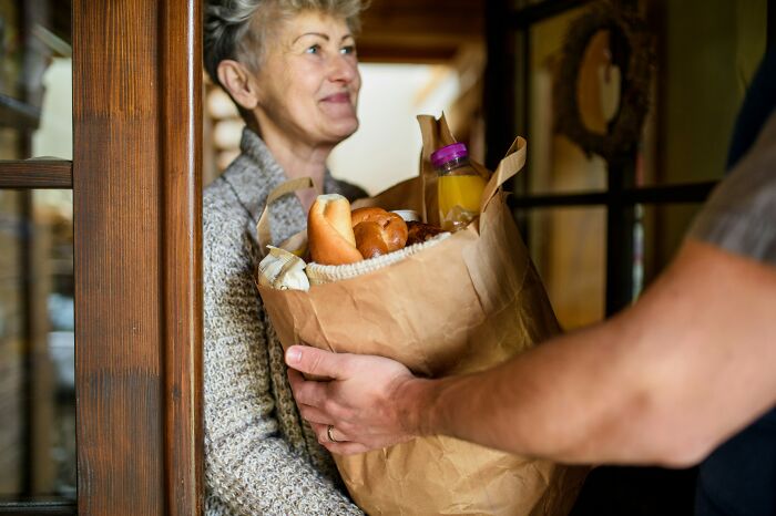 A smiling older woman receives a bag of groceries. This image connects to a last will and testament.