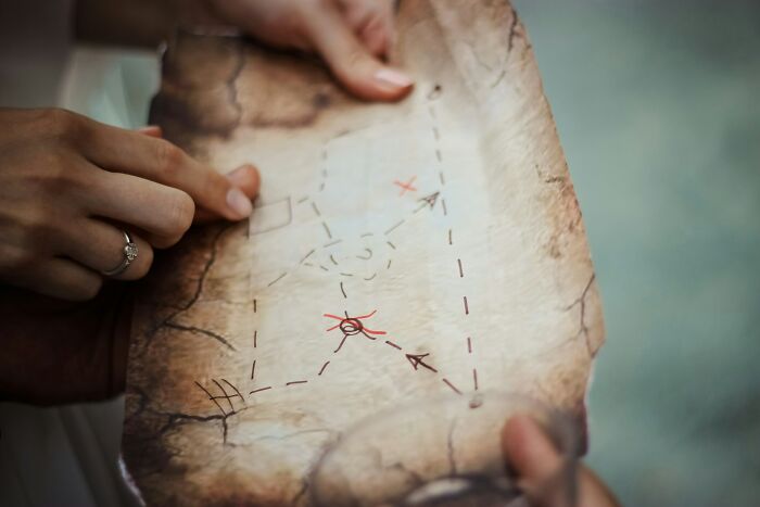 Two hands holding an old, tattered treasure map with an 'X' marking a spot, symbolizing funny last will stories.