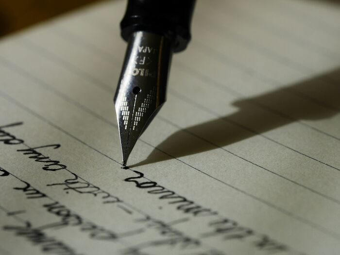 A fountain pen writing on lined paper, representing the act of drafting a last will with funny and serious stories.