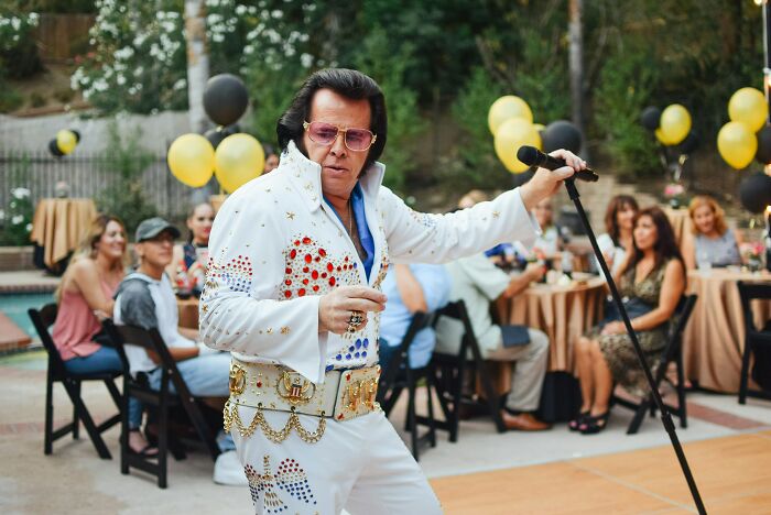 An Elvis impersonator performing outdoors, entertaining guests with funny last will stories.