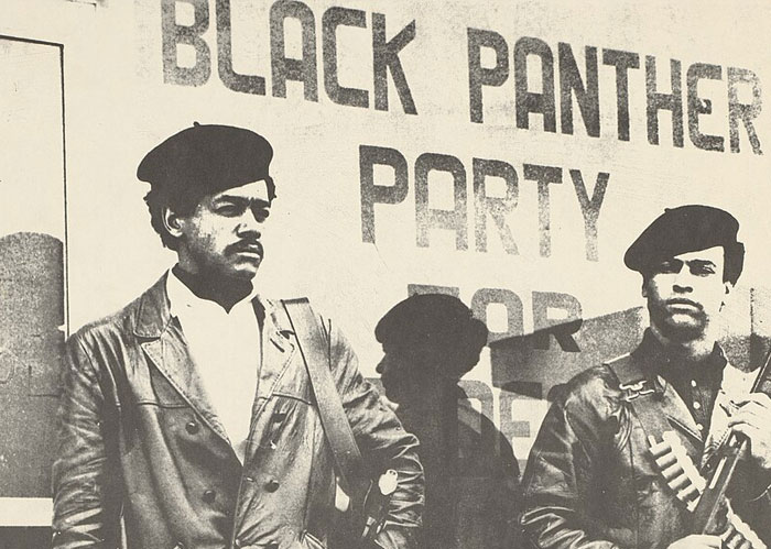 Black Panther Party members standing in front of a banner. Learn interesting facts about America.