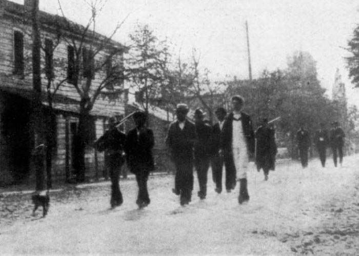 America: Black and white photo of men walking down a dirt road in a historical setting.