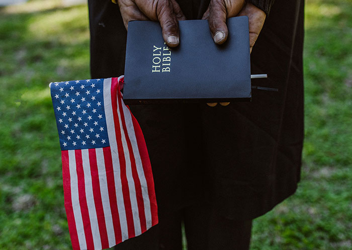 Hands holding a Holy Bible and a small American flag, symbolizing America facts about faith.