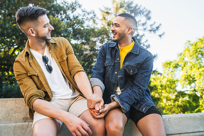Two happy gay men holding hands in a park. This image relates to a groom's family getting banned from a wedding.