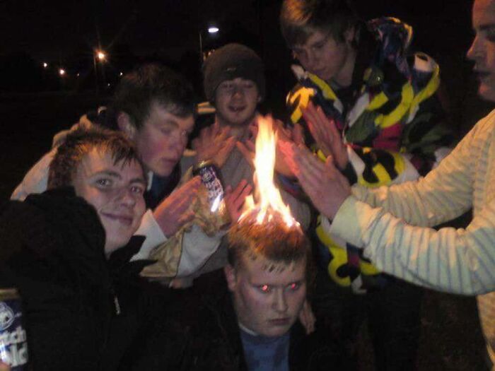 Young men gathered around a friend whose hair is on fire, a confusing image requiring a priest.