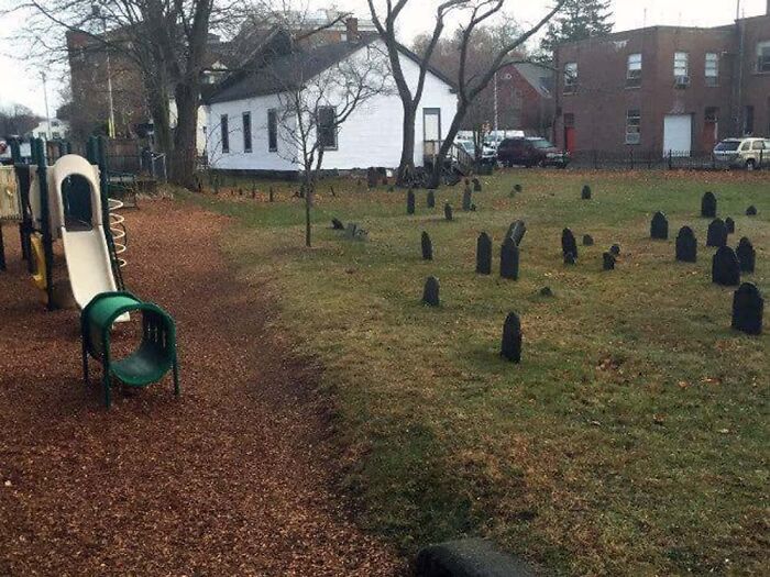 A playground with a slide next to a graveyard, making for a creepy and confusing image.