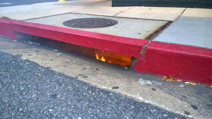 Fire coming out of a street drain, a confusing image that needs a priest.