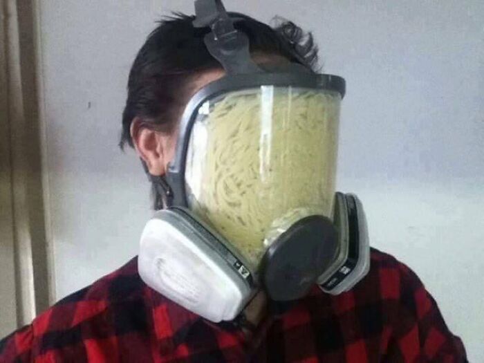 A creepy and confusing image of a person wearing a gas mask filled with spaghetti, needing a priest.