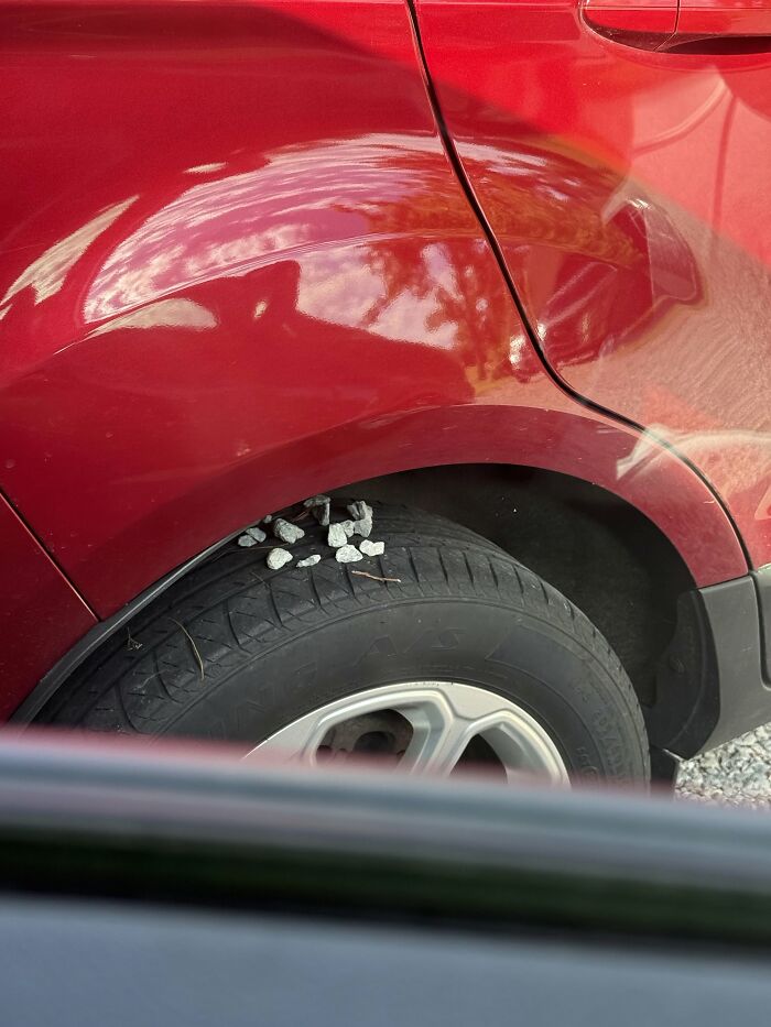 A red car with creepy and confusing small rocks lodged in the tire tread, needing a priest.