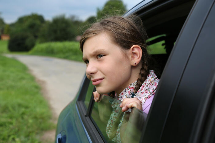 Young girl with braids looking out a car window, representing a childhood experience.