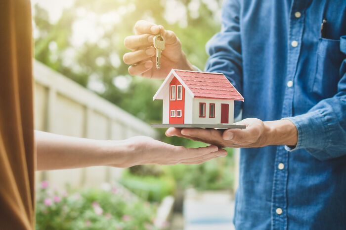 Hands exchanging a small house model and keys, symbolizing a significant childhood experience.