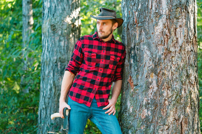 Man in a plaid shirt and cowboy hat leaning against a tree, depicting a childhood experience.
