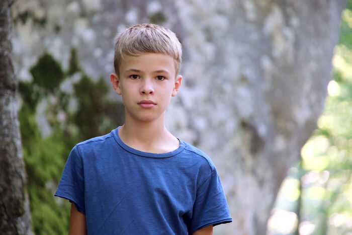 A young boy with short blonde hair looks directly at the camera, conveying childhood experiences.
