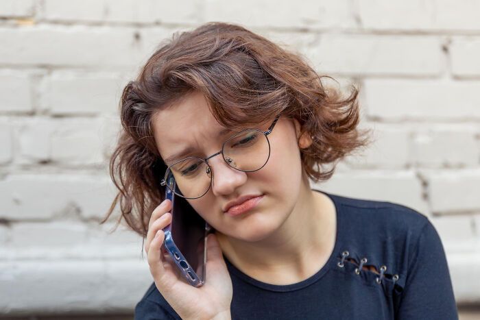 A young woman with glasses on the phone, reflecting on childhood experiences.