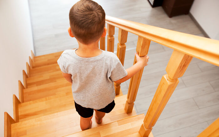 A young boy descending wooden stairs, representing common childhood experiences.