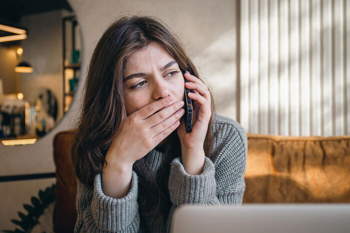 A woman on the phone with a surprised expression, recalling unbelievable childhood experiences.