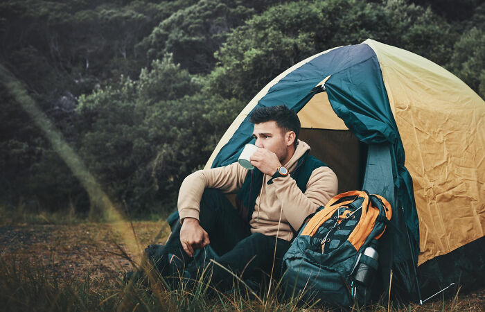 A man sitting outside a tent with a mug, enjoying the outdoors and creating unique childhood experiences.