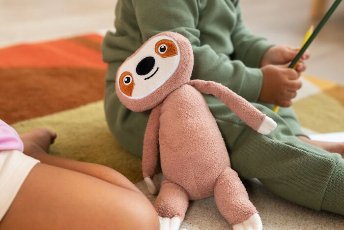 A cute plush sloth sits on a colorful rug next to a child, symbolizing a cherished childhood experience.