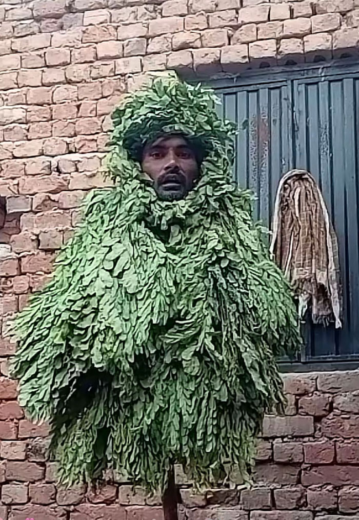 A man in a full body leaf suit, standing against a brick wall, a camera roll photo needing explanation.