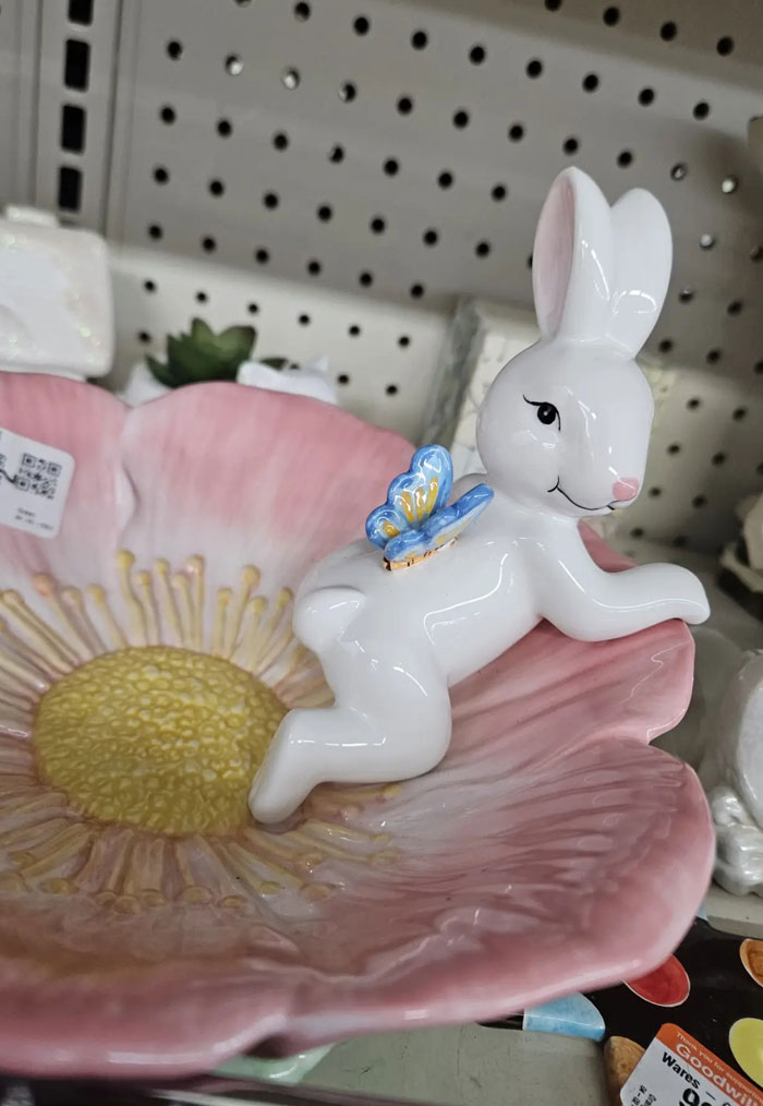 A white ceramic bunny with a blue butterfly on its back, sitting on a pink floral dish, a strange camera roll photo.