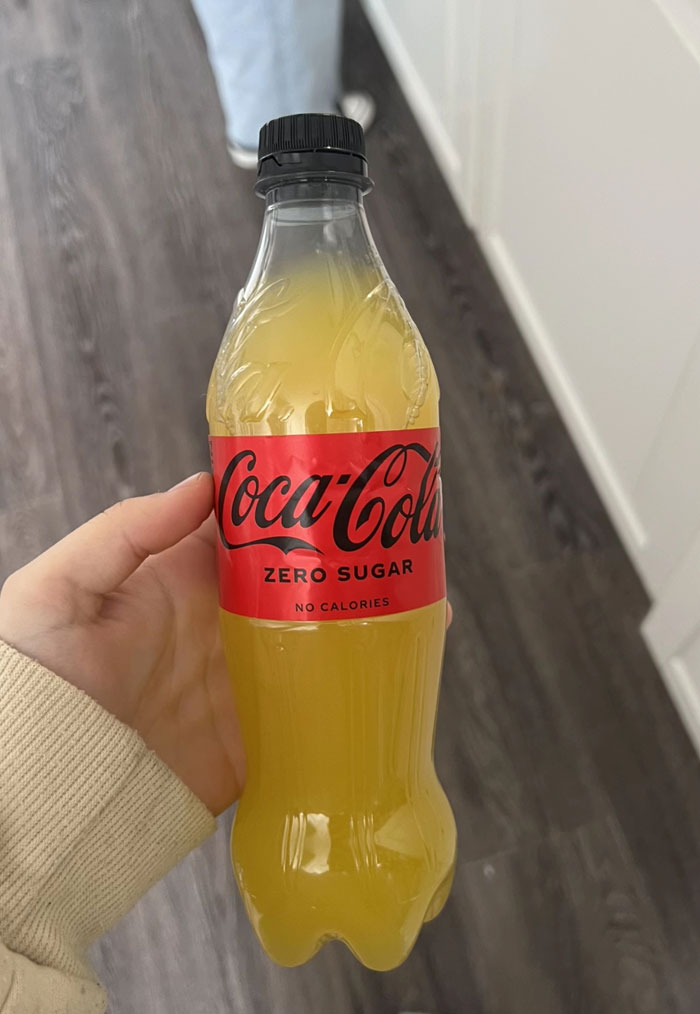 A hand holding a Coca-Cola Zero Sugar bottle filled with a yellow liquid, a camera roll photo.