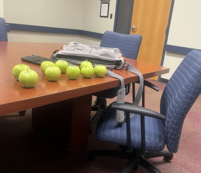 A conference table covered with many green apples and a bag, a surprising camera roll photo.