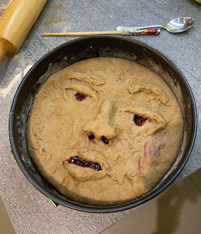 A creepy face made of dough in a baking pan, featuring red jam for eyes and mouth, one of many camera roll photos.