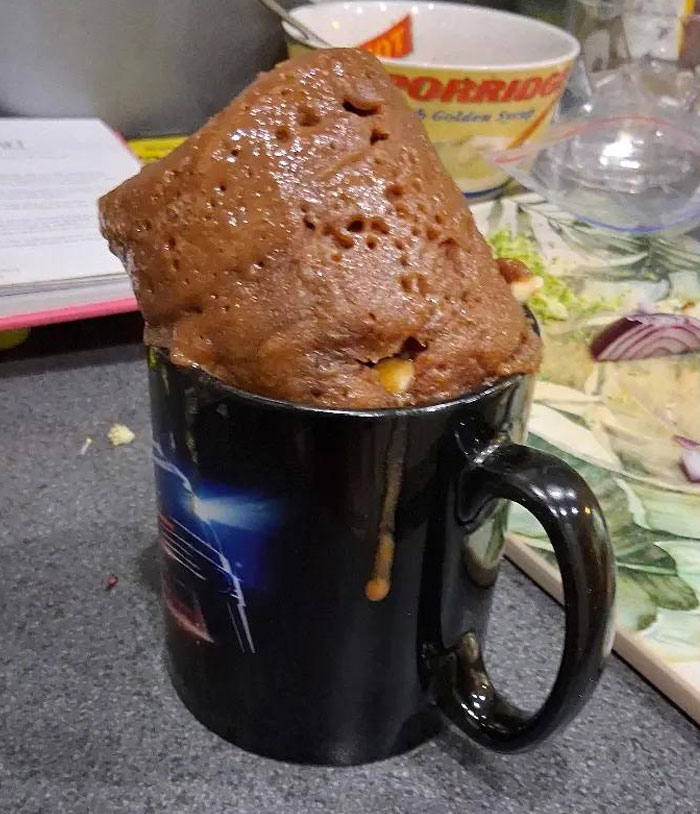 An overflowing chocolate mug cake in a black mug, a funny camera roll photo that needs no explanation.