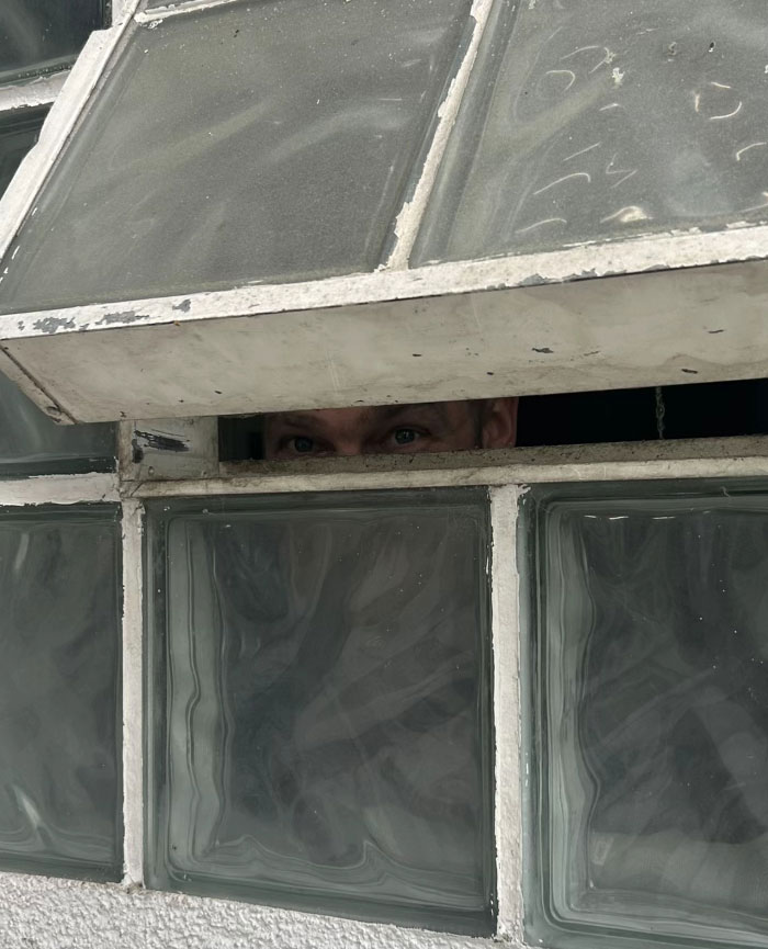 Camera roll photos reveal two eyes peering over a half-open, dirty glass block window, suggesting someone is looking in or out.
