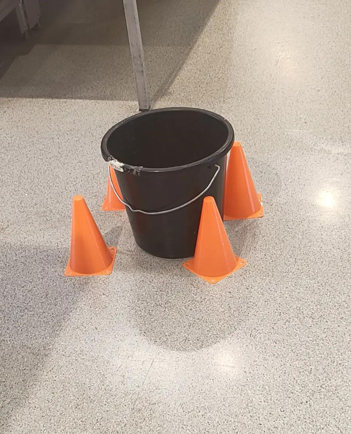 A black bucket surrounded by four orange traffic cones, a puzzling camera roll photo.