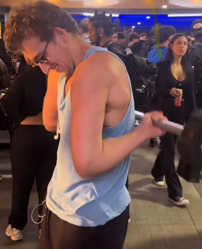 A man in a light blue tank top flexing his bicep in a crowd, a camera roll photo needing explanation.