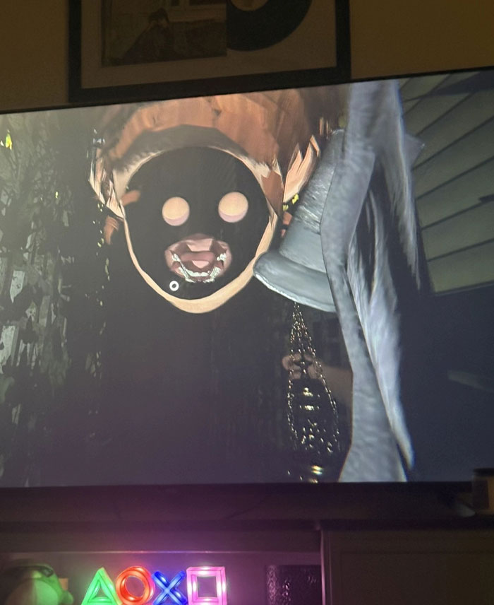 A screen displaying a dark, unsettling character from a video game with a mask and glowing eyes, a mysterious camera roll photo.