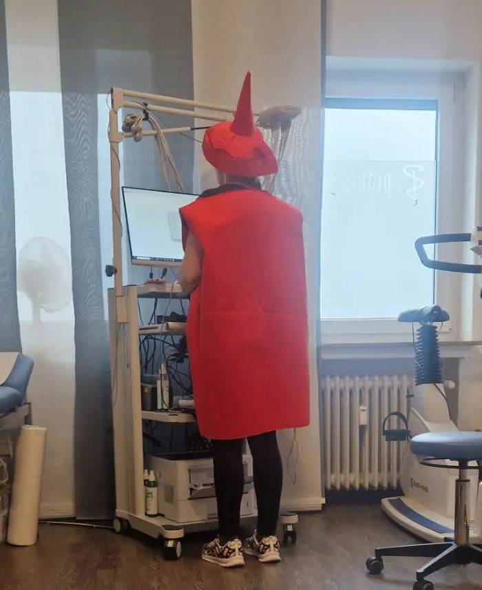 A person in a bright red, cone-hatted costume standing in a medical office, a peculiar camera roll photo.