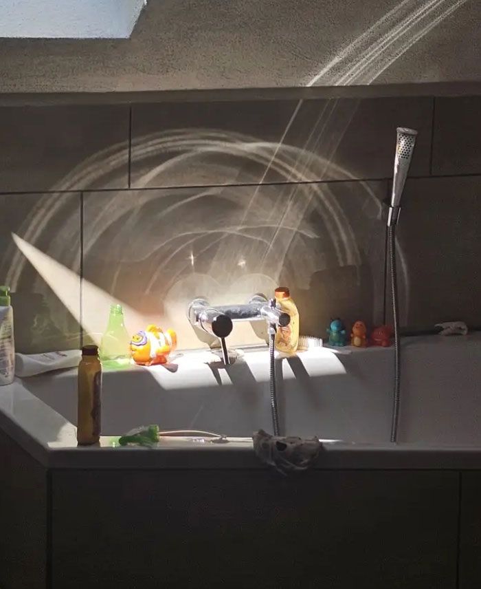 A camera roll photo of light rays creating circular patterns on a tiled bathroom wall above a bathtub.