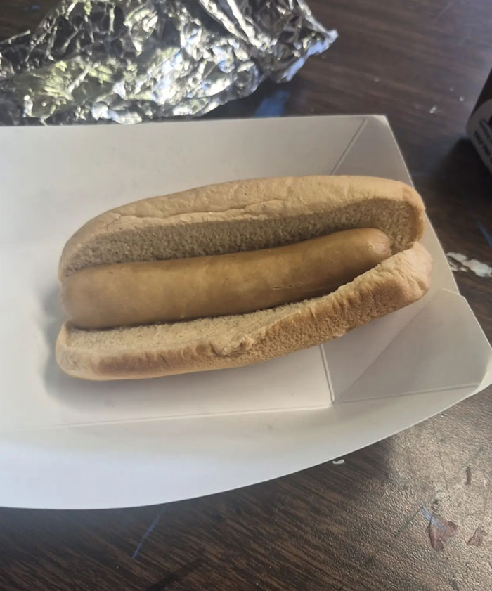 A plain hot dog in a bun, served in a white cardboard tray from camera roll photos.