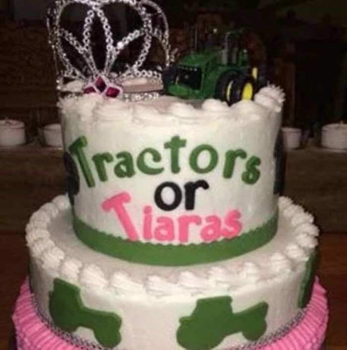 A two-tiered gender reveal cake decorated with Tractors or Tiaras, topped with a tiara and toy tractor.