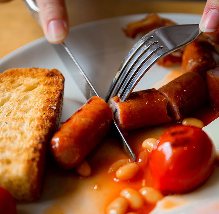 Person cutting a sausage on a plate with beans and toast, illustrating a culture shock in intercultural relationships.