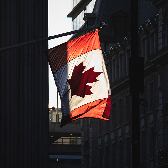 A Canadian flag waving against a backdrop of city buildings, representing cultural identity and potential culture shocks.