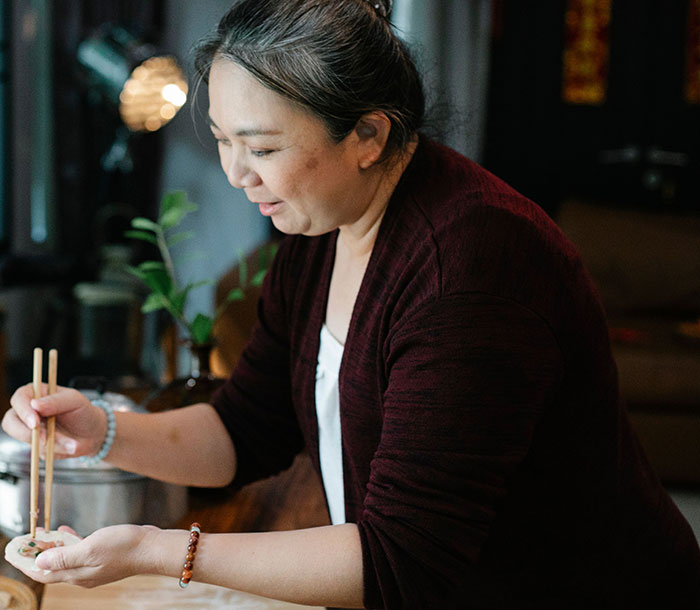 An Asian woman preparing food with chopsticks, showcasing a moment of cultural sharing in intercultural relationships.