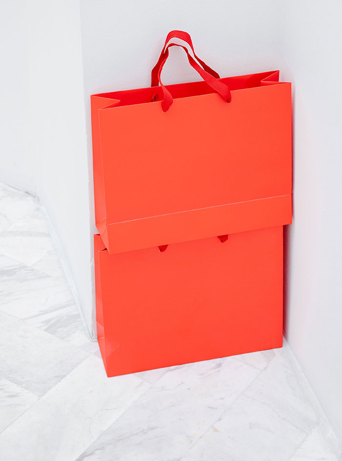 Two vibrant red shopping bags against a white wall and marble floor, showcasing aspects of intercultural relationships.