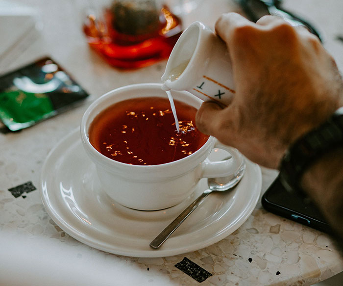 A hand pouring milk into a cup of tea, symbolizing daily interactions and potential culture shocks.