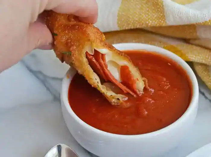 A hand dipping a crispy snack into red sauce, a relatable moment that can lead to discussions about culture shocks and intercultural relationships.