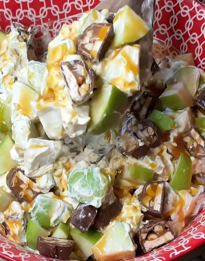 Dessert salad with apples, whipped cream, and candy bars in a red bowl, representing a challenging culture shock.