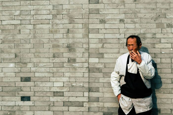 A man smoking against a brick wall, reflecting on culture shock.