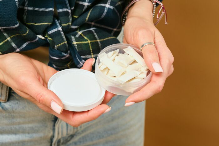 Hands holding an open container of nicotine pouches, a product that might cause culture shock for some travelers.