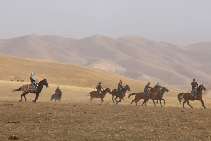 Travelers on horseback riding through a dry, mountainous landscape, an unexpected cultural experience.