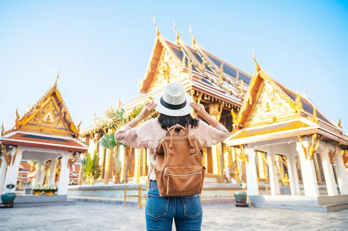 A traveler with a hat and backpack admiring a golden temple, experiencing the wonders of culture shock.